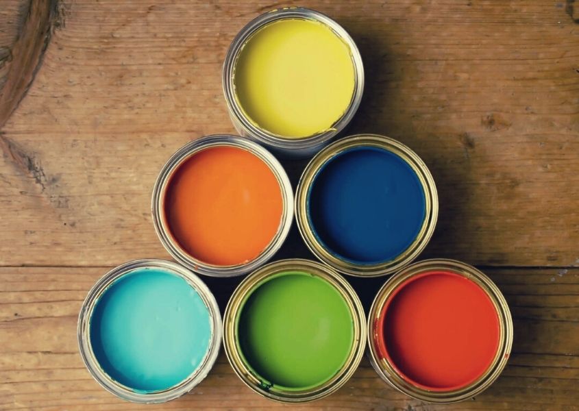 Six small paint pots with different coloured paints inside on wooden table