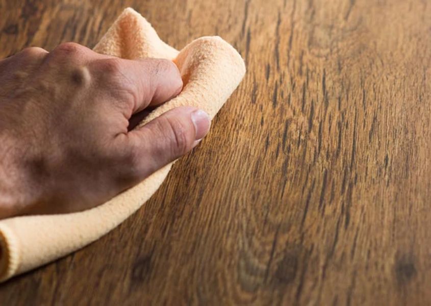 cleaning top of a rustic dining table with a yellow cloth