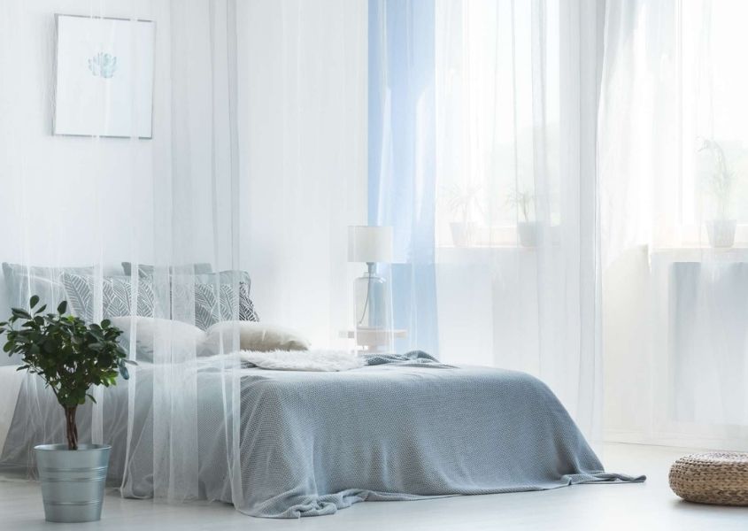 Grey double bed with sheer white curtains