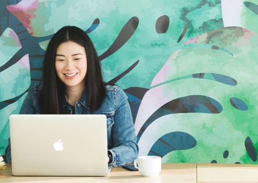 woman sat at desk with large green palm mural on wall behind