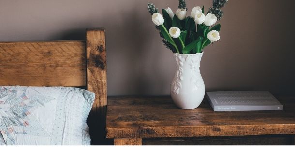 Wooden double bed with matching bedside table with white vase and flowers