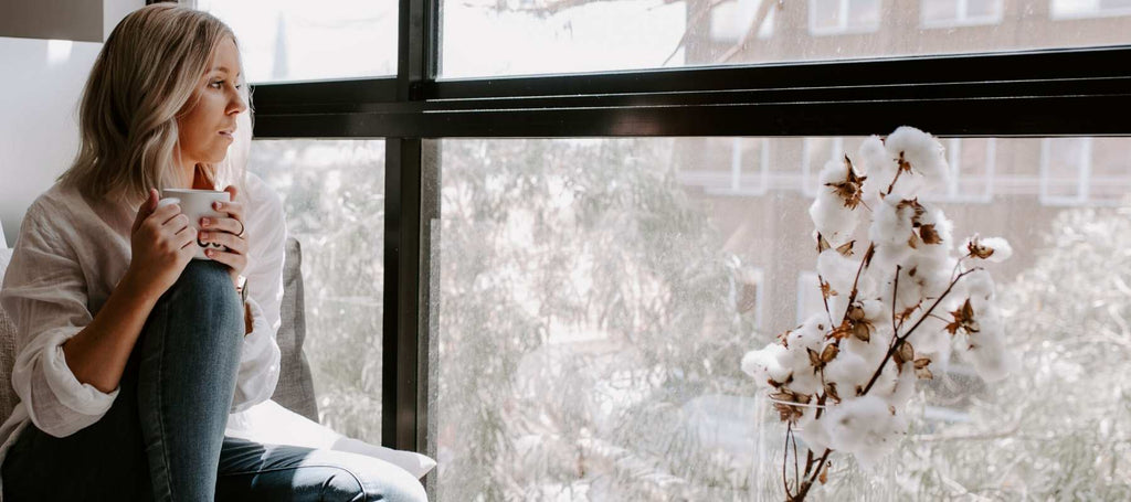 Woman sat in sunny window holding a cup of tea