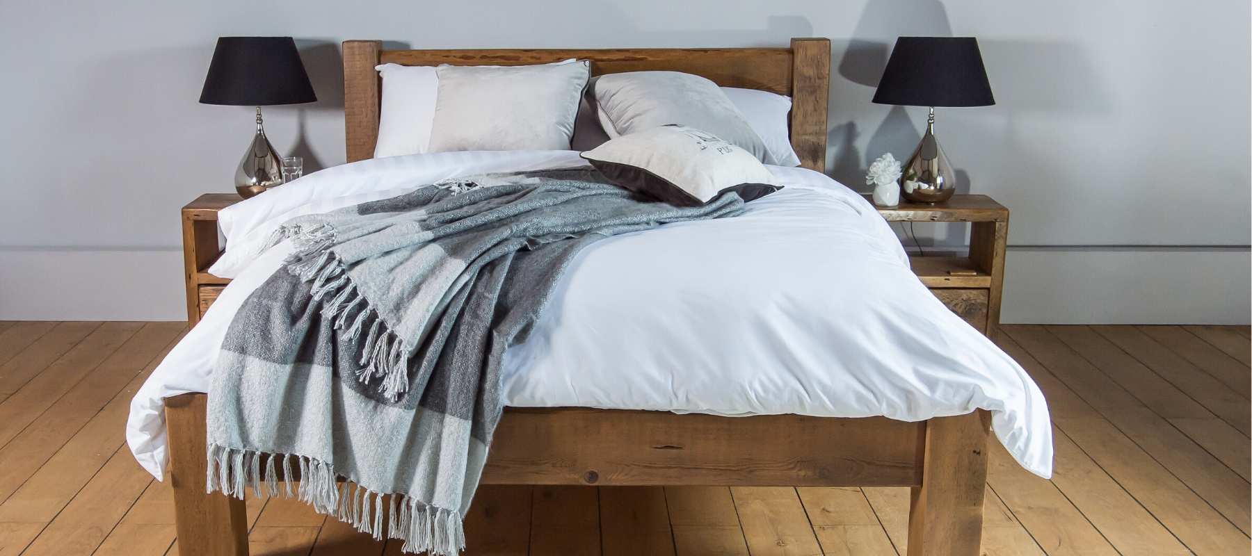 Wooden double bed frame with white covers and grey blanket