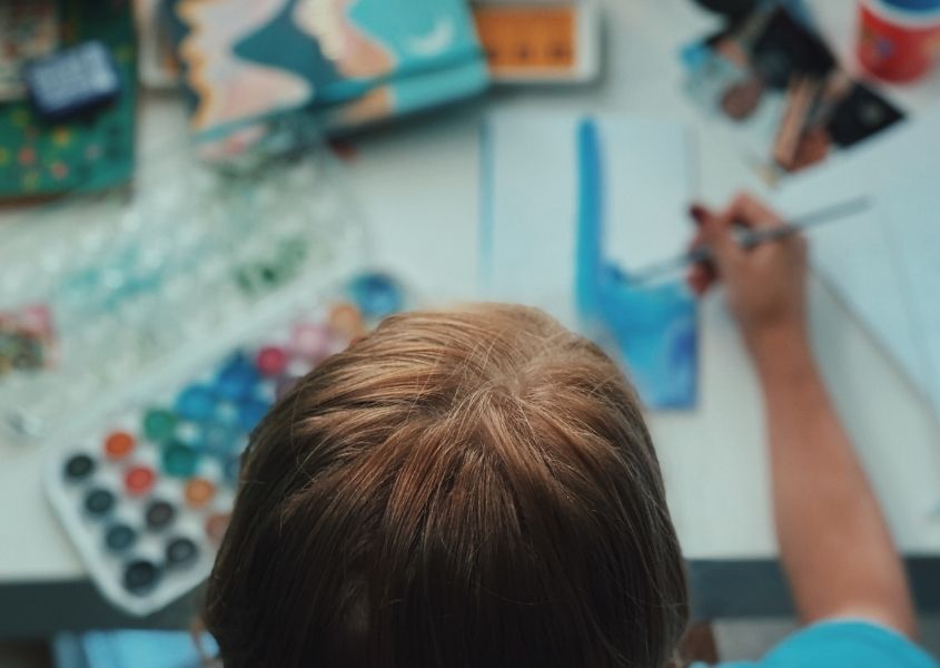 child at white wooden desk drawing and painting