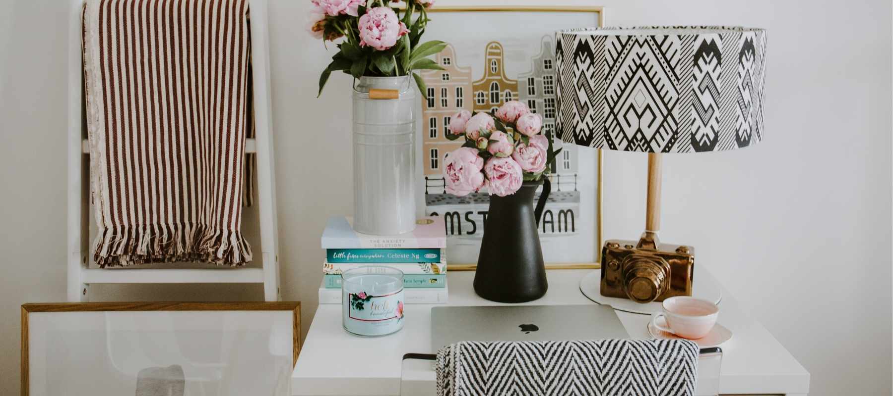 White desk with table lamp, flowers and striped blanket
