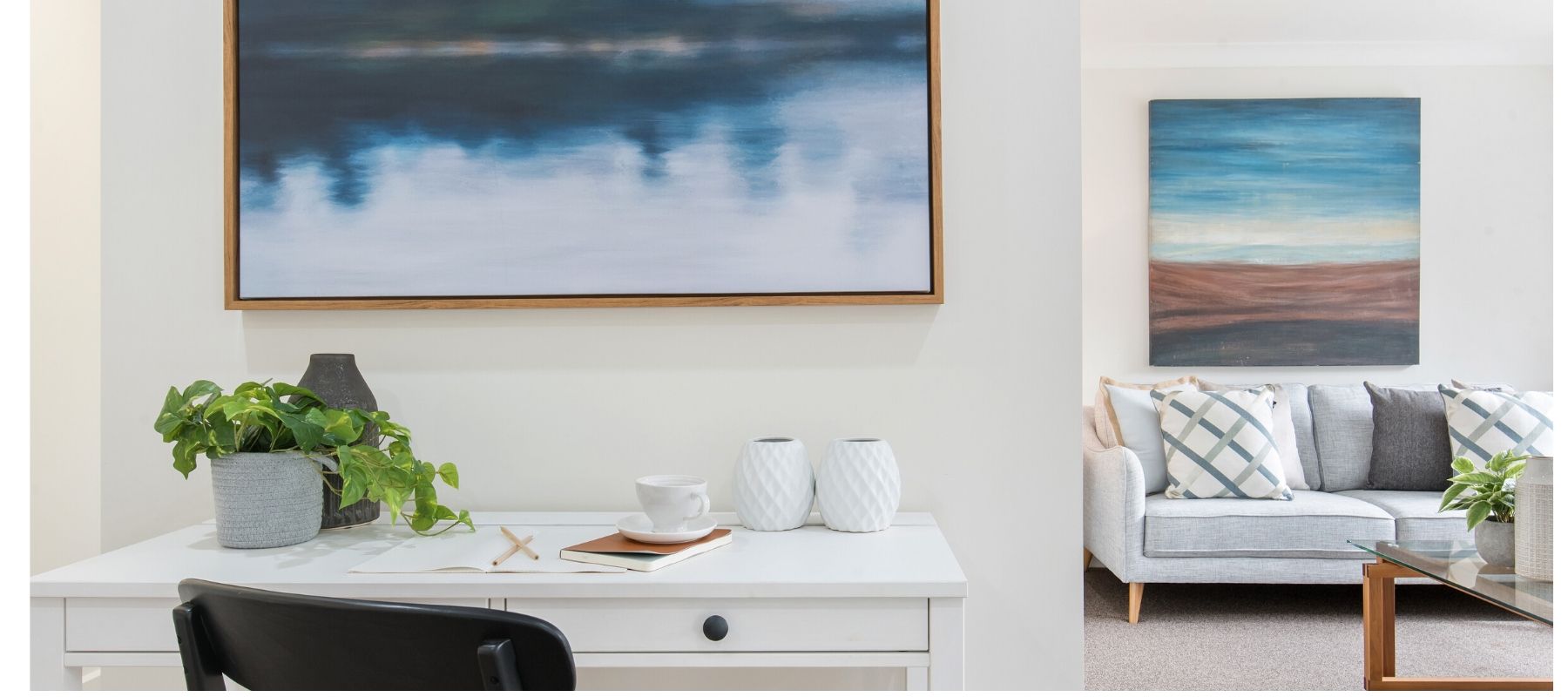 White desk with blue wall art and grey sofa