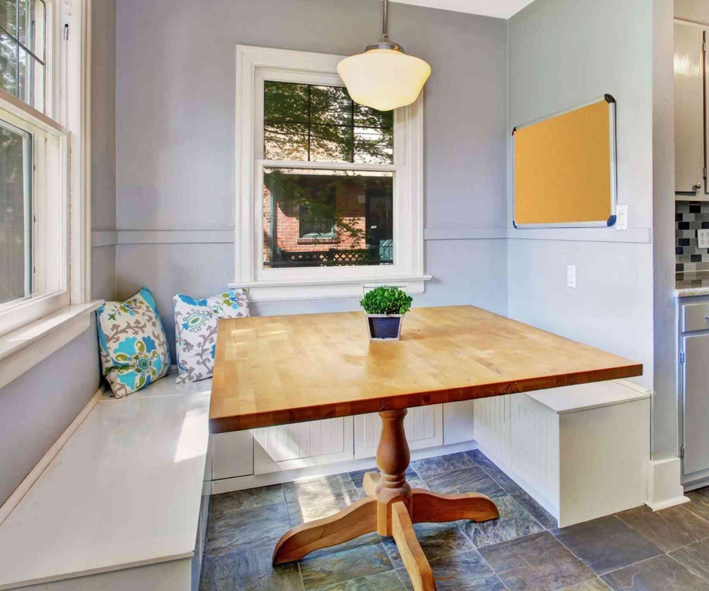 Square wooden dining table in corner of dining room with wraparound bench