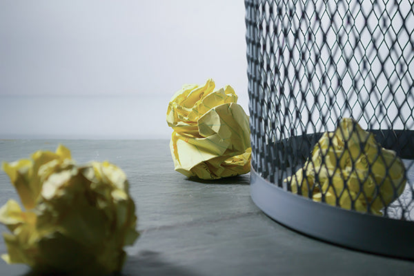 Three pieces of yellow paper through near a paper bin