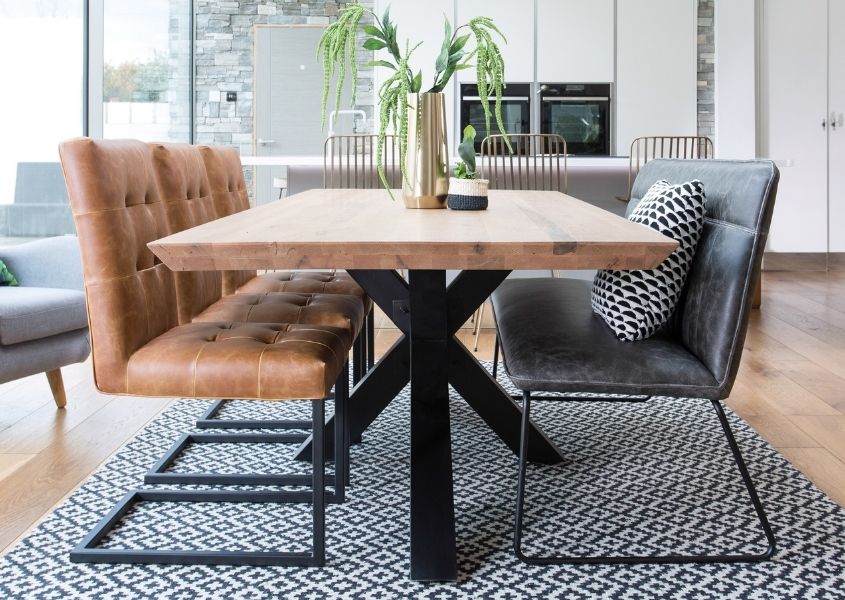 Industrial dining table with thick black steel spider leg base and three tan leather dining chairs with black legs and grey faux leather dining bench