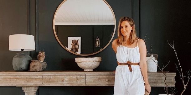 Women in white dress standing in front of large rustic console table with round mirror on wall