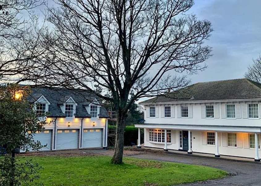Exterior of white colonial style home with separate garage and large tree in front garden