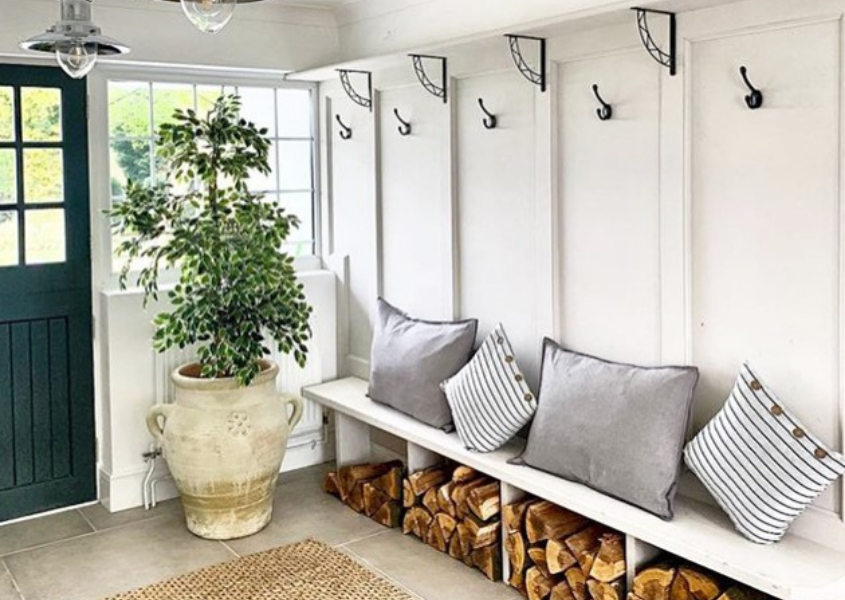 Boot room with white bench and logs underneath and large stone pot with plant