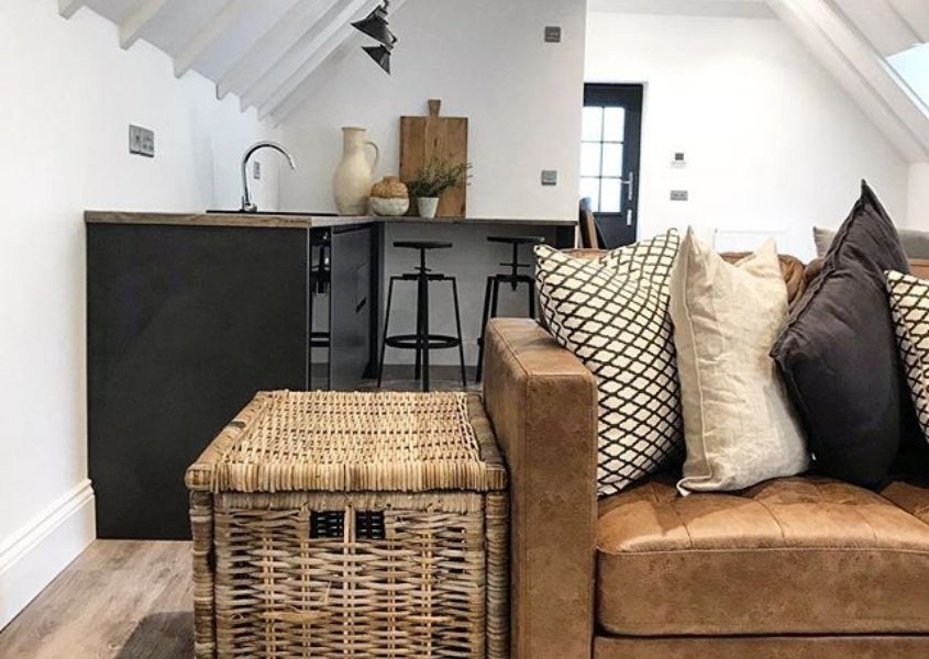 Brown leather sofa with large basket side table and small blue kitchen in background