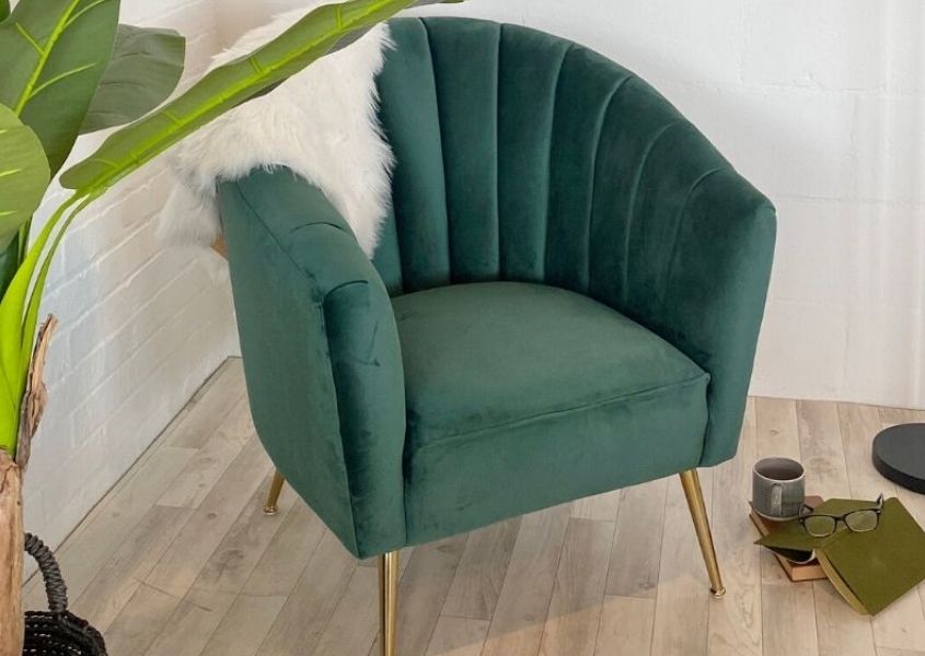 Green velvet armchair next to green plant and books and cup on floor