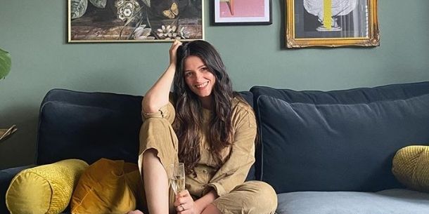 Woman with long dark hair sat on dark blue velvet sofa