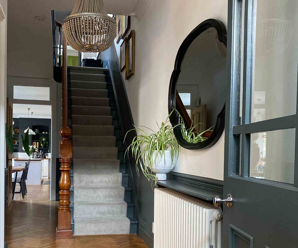 View from hallway up staircase with round wall mirror and white carpet runner up stairs