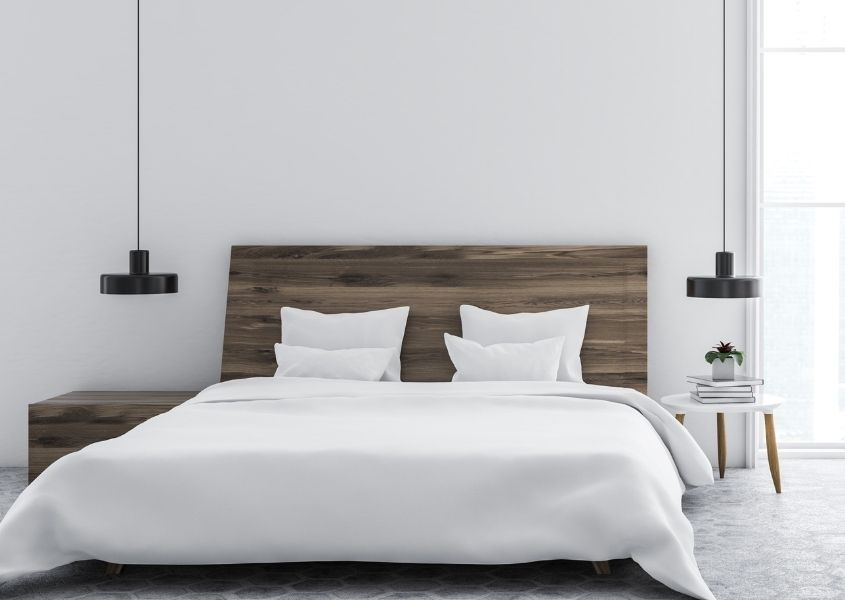 White bedroom with wooden double bed and white covers with a pendant ceiling lights each side