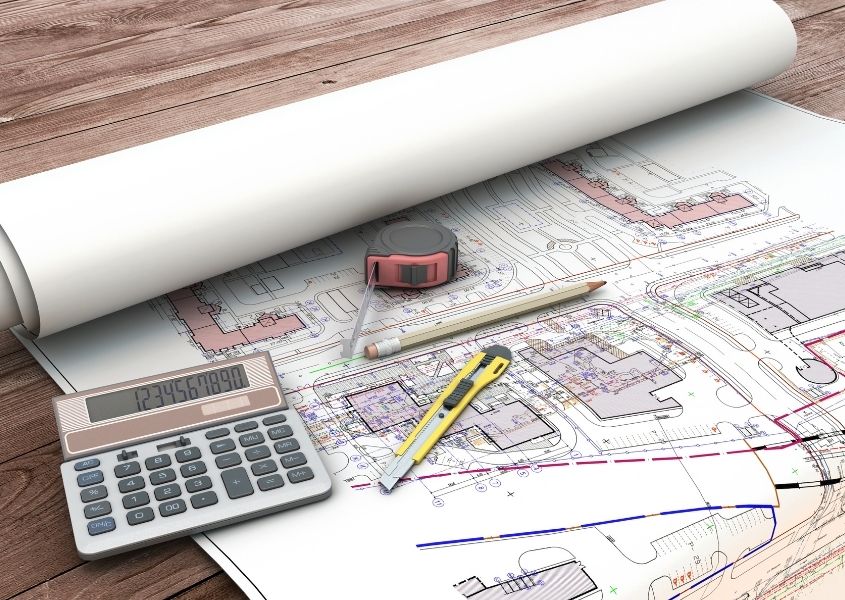 Building plans on a wooden table with a calculator and pencil