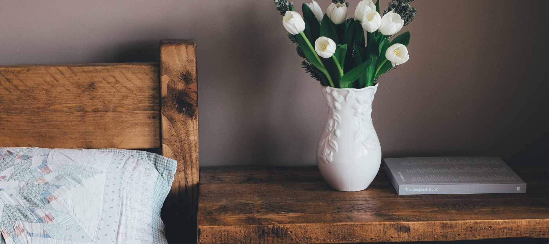 Wooden bed and bedside table with white vase and flowers