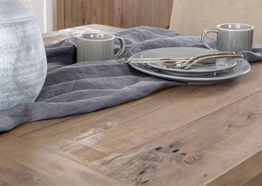 Close up of reclaimed wood dining table with grey linen runner, plates and grey stone vase