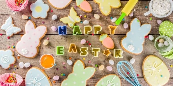 Happy Easter words on a rustic wood table with iced biscuits cut in shape of rabbits and baking utentils