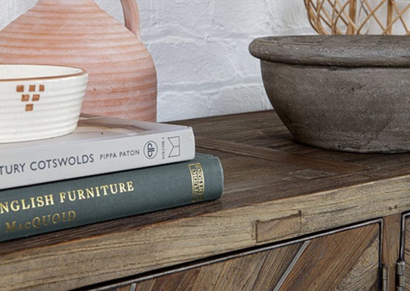 Close up of pile of books and terracotta vase on top of wooden sideboard 