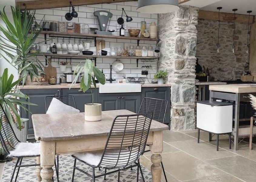 Square reclaimed wood dining table in kitchen with grey cabinets and rustic open shelves