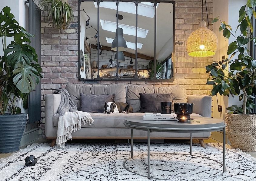 Grey sofa with white and black rug against a stone wall with a large leaded mirror