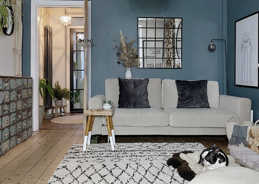 Living room with blue painted wall and large paneled mirror with cream sofa and wooden milking stool