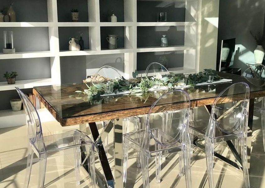 Reclaimed wood dining table with rustic wood and glass top with clear plastic dining chairs and plant table decoration