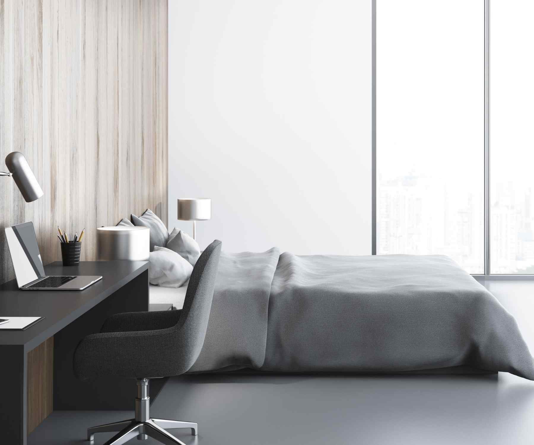 Large bed with grey bed covers and a desk in a bedroom