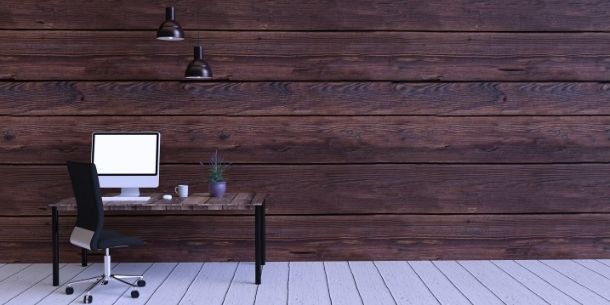 Reclaimed wood desk with black metal legs and modern office chair in a large empty room with wide rustic wood panelling on the walls
