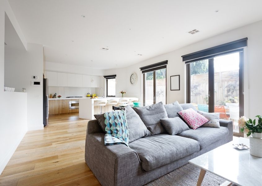 Open plan kitchen and living room with white kitchen, wooden floor and grey fabric sofa with large patio doors