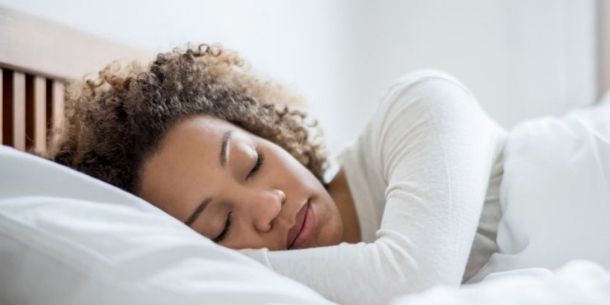 Woman in long sleeved white t-shirt asleep in wooden bed with white covers