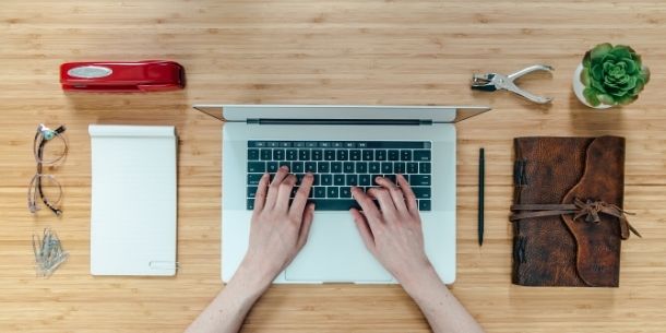 Woman's hands typing at a lap top with tidy accessories on wood desk