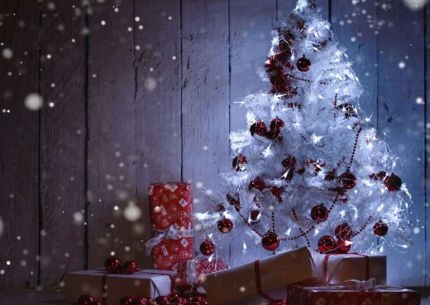 Lit up white Christmas trees with presents underneath in dark room