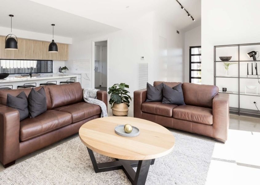 two brown leather sofas and round wooden coffee table with black metal legs