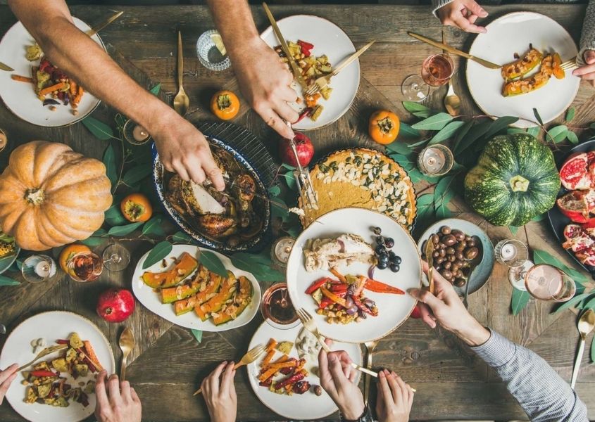 Close up of lots of different autumnal foods on a wooden dining table with people's arm serving