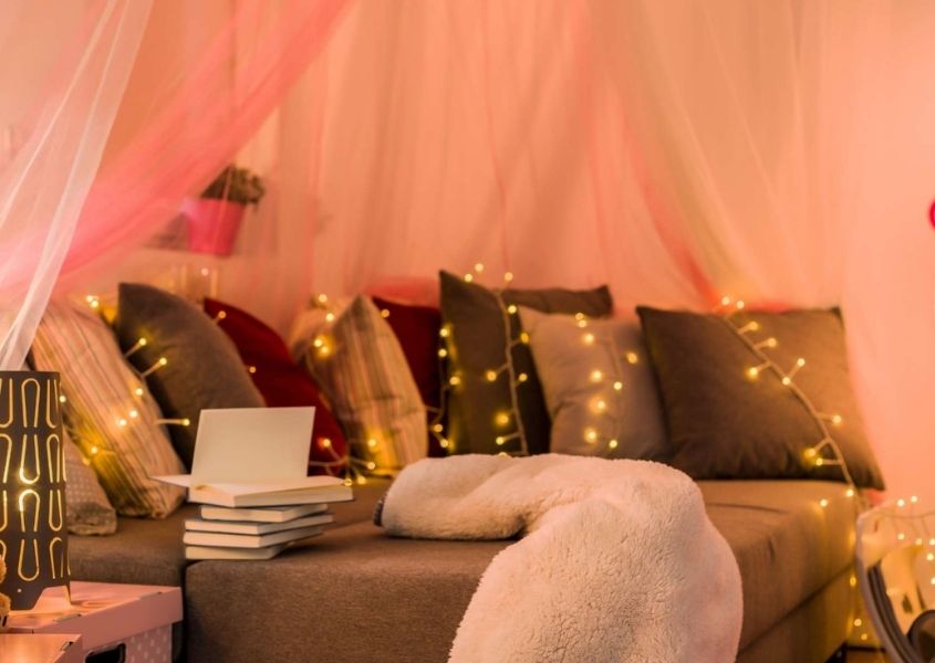 Bed with lots of cushions under sheer pink drapes