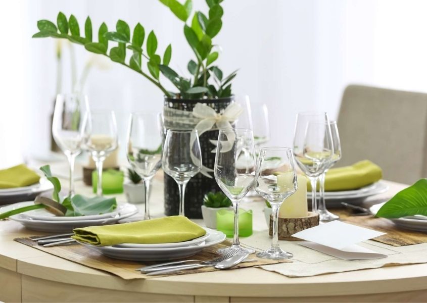 Blue and white tall vase with green leaves on wood dining table with white plates and green linens