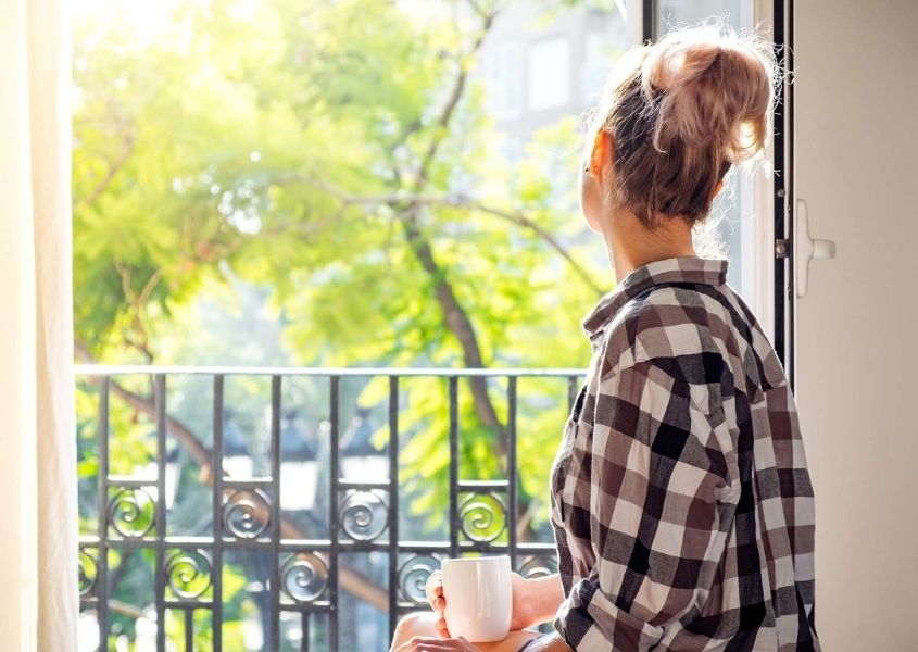 Girl sat at open window in living room looking out to green trees