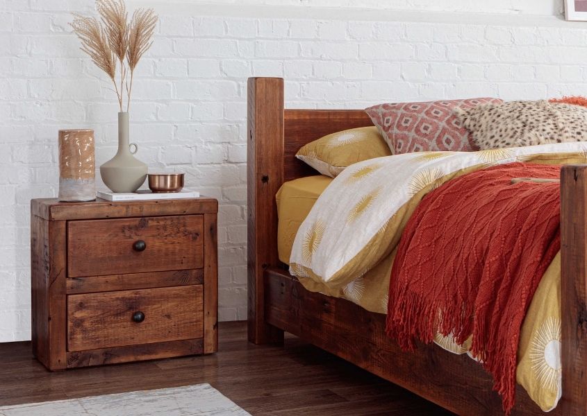 wooden bedside table with jug and vase of dried plants