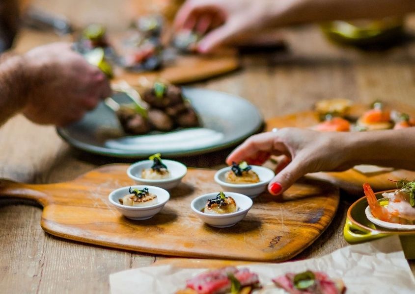 Wooden serving board with canapes on and handing picking up food on wooden dining table
