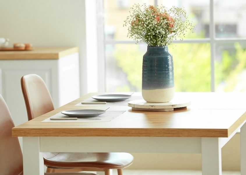 Wood dining table with white painted legs and blue and white vase on wooden coaster in centre of the table
