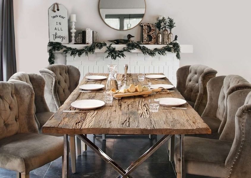 Reclaimed wood dining table with silver legs and taupe upholstered dining chairs in front of Christmas decorated fireplace