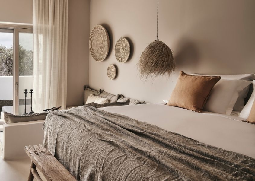 rustic wooden bench at foot of king size bed with natural covers at hotel Habitat, Mykonos