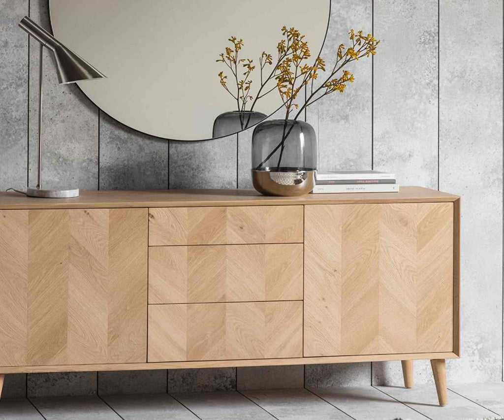 Pale wood sideboard and round mirror with glass vase and orange autumn flowers