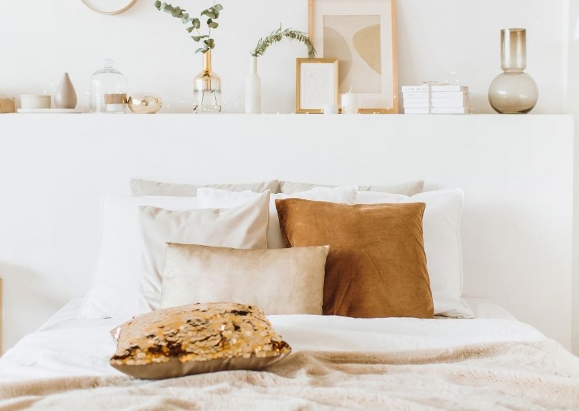 White bed covers with orange cushion ornaments on wooden headboard