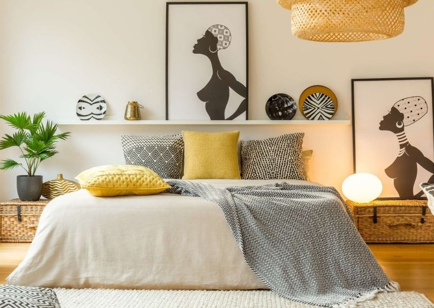 Large king size bed with white, yellow and grey covers and cushions and artwork on the walls