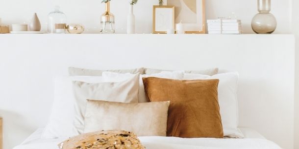 White bedcovers with gold and white cushions and ornaments on shelf behind